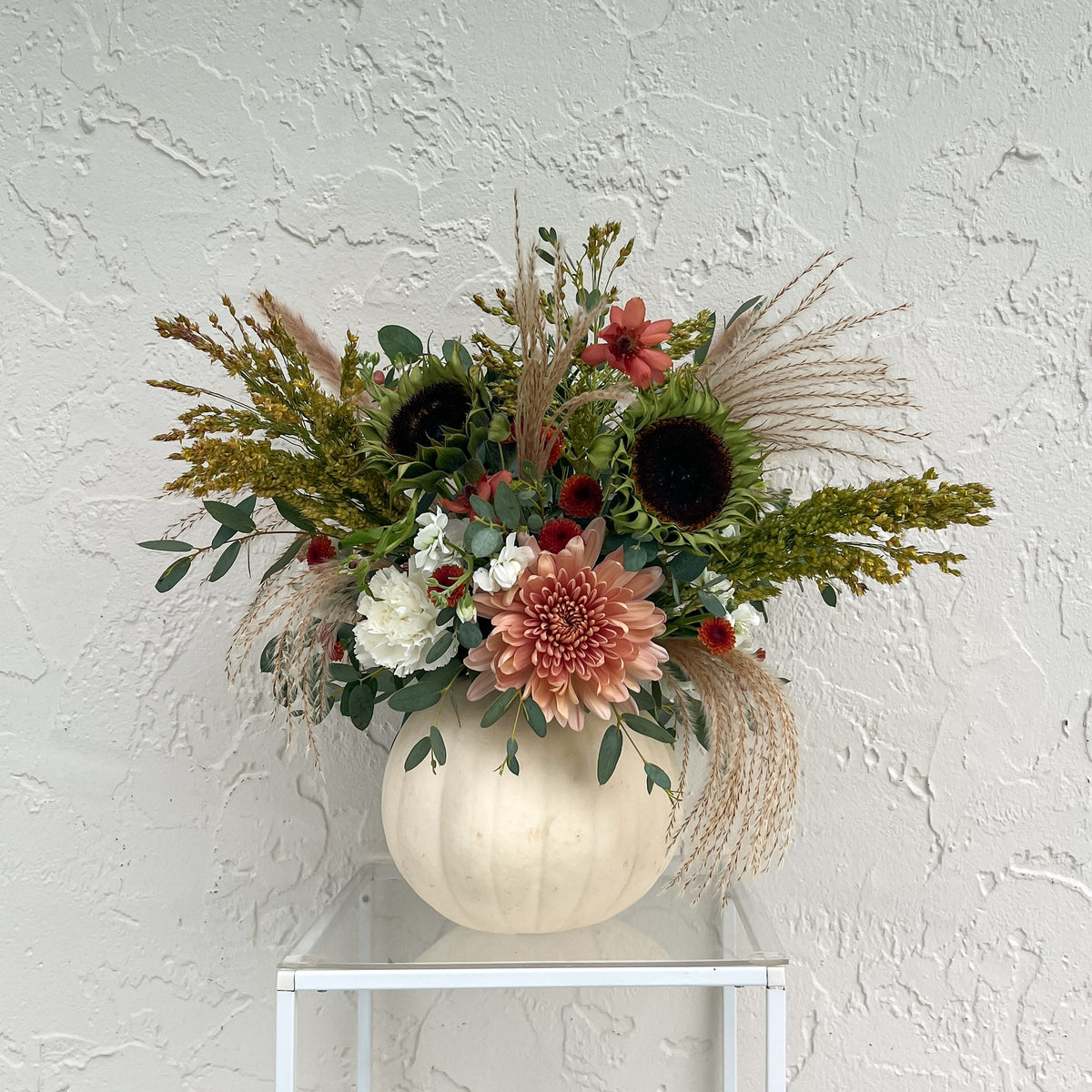 White pumpkin filled with fresh cream and dusty pink flowers, sunflowers, eucalyptus, and cascading pampas grass.