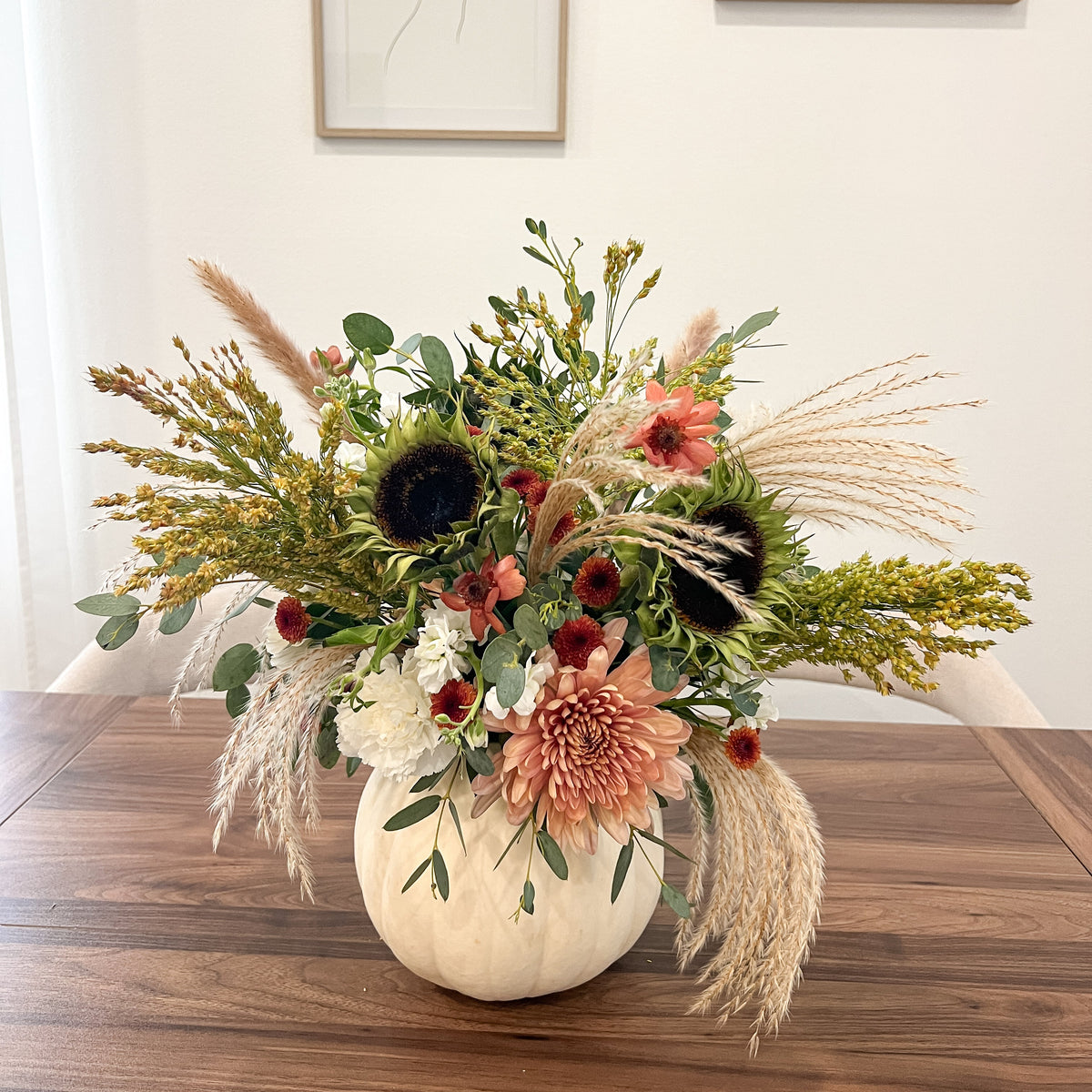 White pumpkin filled with fresh cream and dusty pink flowers, sunflowers, eucalyptus, and cascading pampas grass.