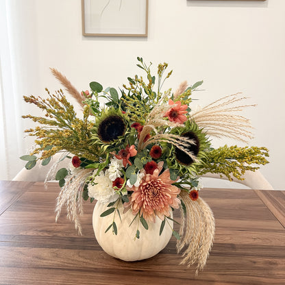 White pumpkin filled with fresh cream and dusty pink flowers, sunflowers, eucalyptus, and cascading pampas grass.