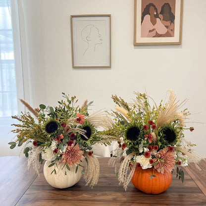 Fresh fall flower arrangements in white and orange pumpkins with cream and dusty pink blooms, sunflowers, greenery, and pampas grass.