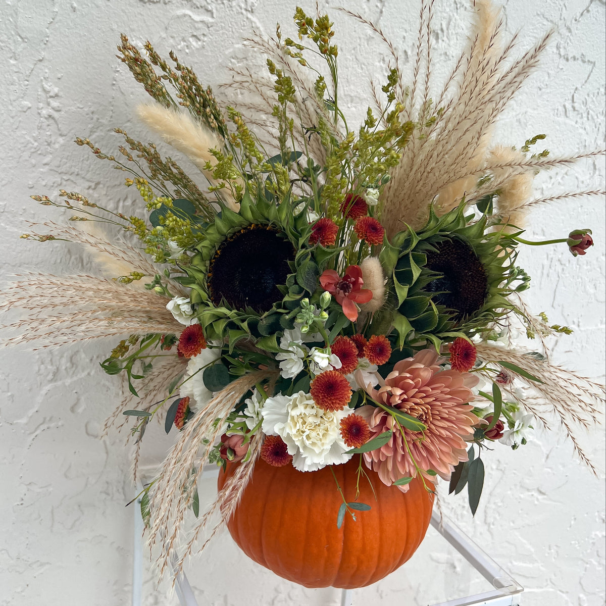 Orange pumpkin filled with fresh sunflowers, dusty pink and cream blooms, burgundy accents, greenery, and pampas grass.