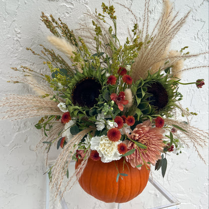 Orange pumpkin filled with fresh sunflowers, dusty pink and cream blooms, burgundy accents, greenery, and pampas grass.