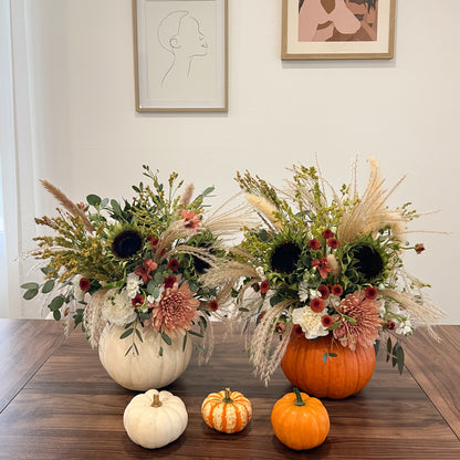 Fresh fall flower arrangements in white and orange pumpkins with cream and dusty pink blooms, sunflowers, greenery, and pampas grass.