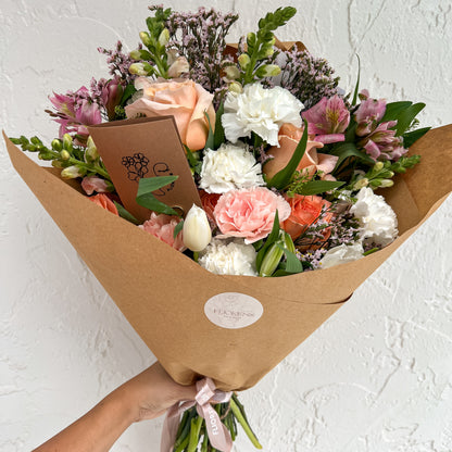 Bouquet of flowers wrapped in brown paper with a visible brand logo against a white background